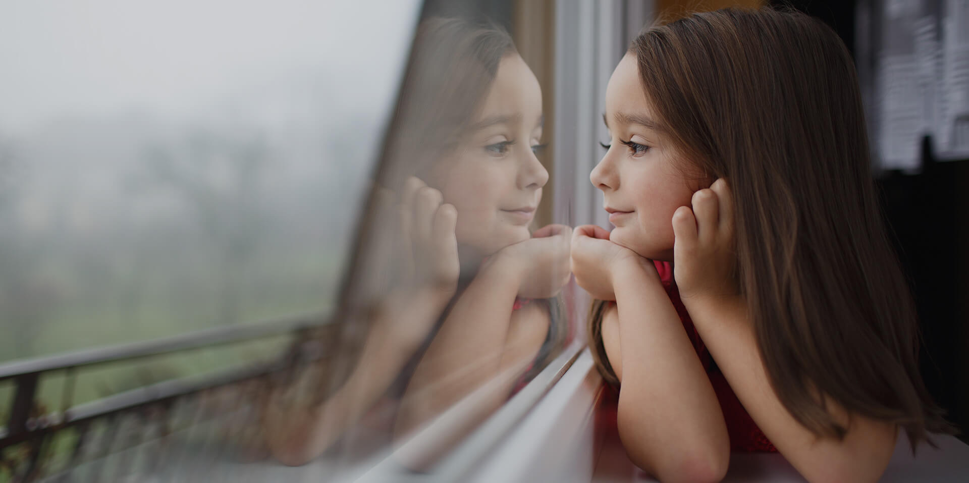 Photo d’atmosphère montrant une enfant regardant par la fenêtre, ainsi que son reflet